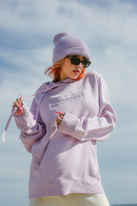 Model in lavender pink hoodie and matching beanie, beach background - PowderLA